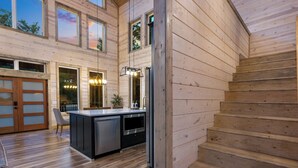 A modern kitchen with wooden walls, a central island, and a staircase leading to an upper level. - 3BR Forest Hideaway! Playset, Pool Table, Foosball (Broken Bow)