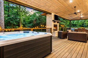 A hot tub on a wooden deck with a stone fireplace and outdoor furniture. - Playset & Pool Table | Hot Tub | Sleeps 14 (Broken Bow)