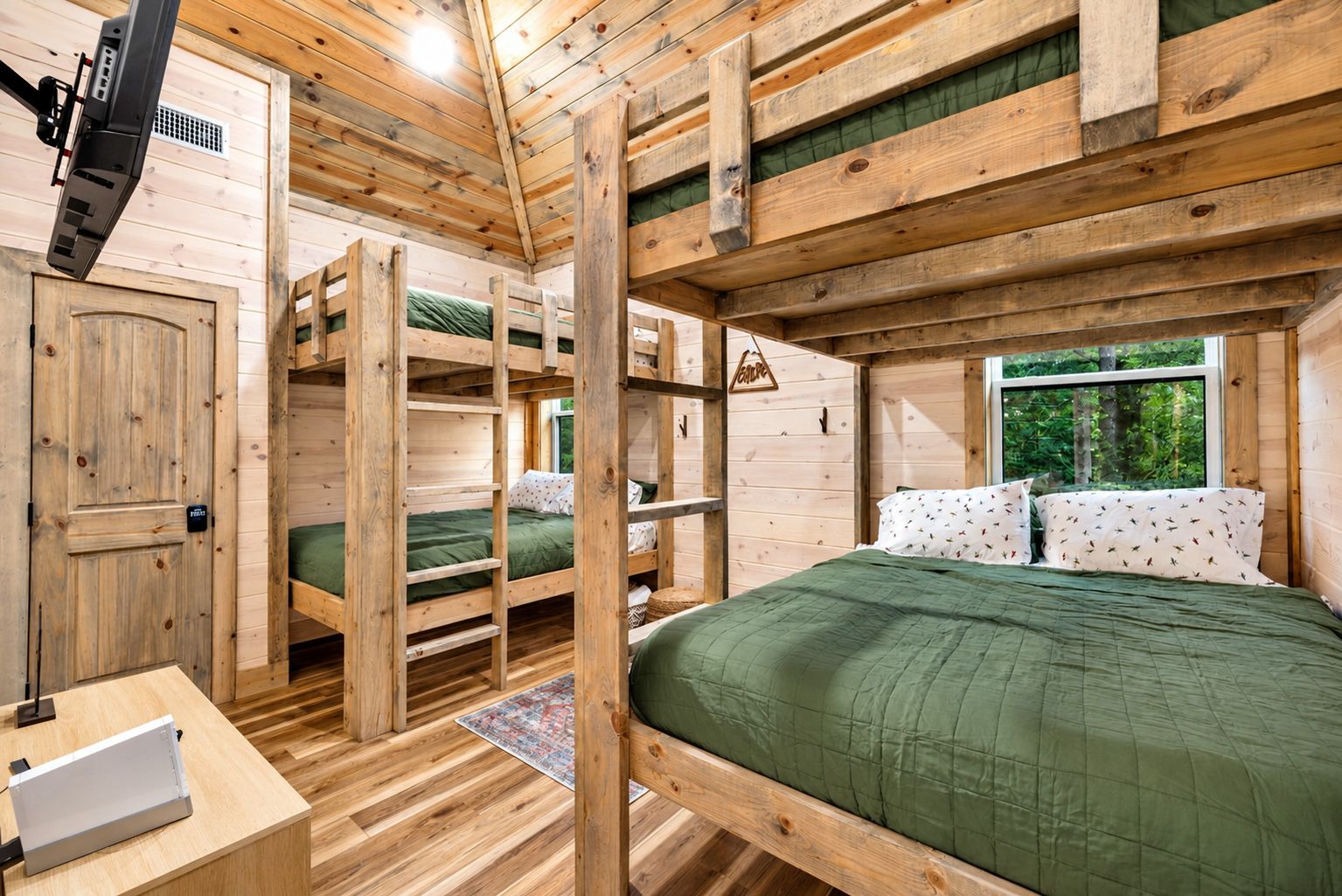 A cabin interior with bunk beds, a wooden desk, and a window with a view of greenery.