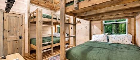 A cabin interior with bunk beds, a wooden desk, and a window with a view of greenery.