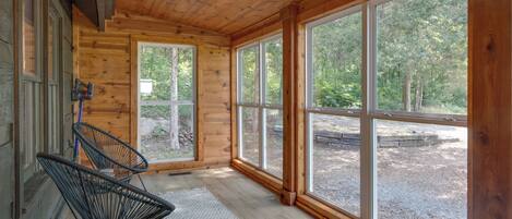 A wooden cabin interior with large windows, a white rug, and two black chairs.