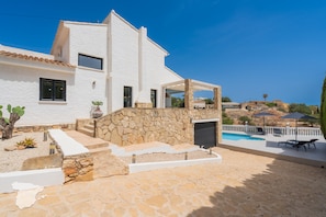 A two-story white house with a stone wall, a swimming pool, and outdoor seating.