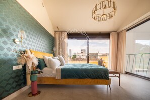 Un dormitorio con cama, mesita de noche, lámpara, ventana y vistas al exterior.