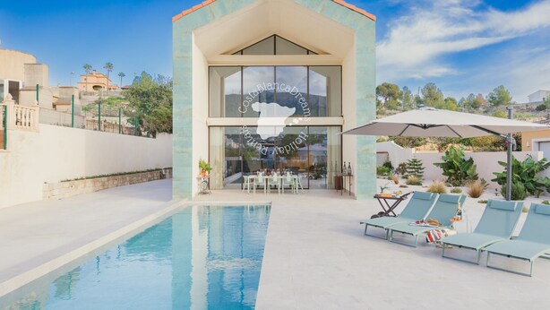 Uma casa moderna com piscina, área de refeições e cadeiras de descanso.