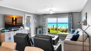 A living room with a large TV, comfortable seating, and a view of the ocean. - Emerald Dunes 103 (Destin)