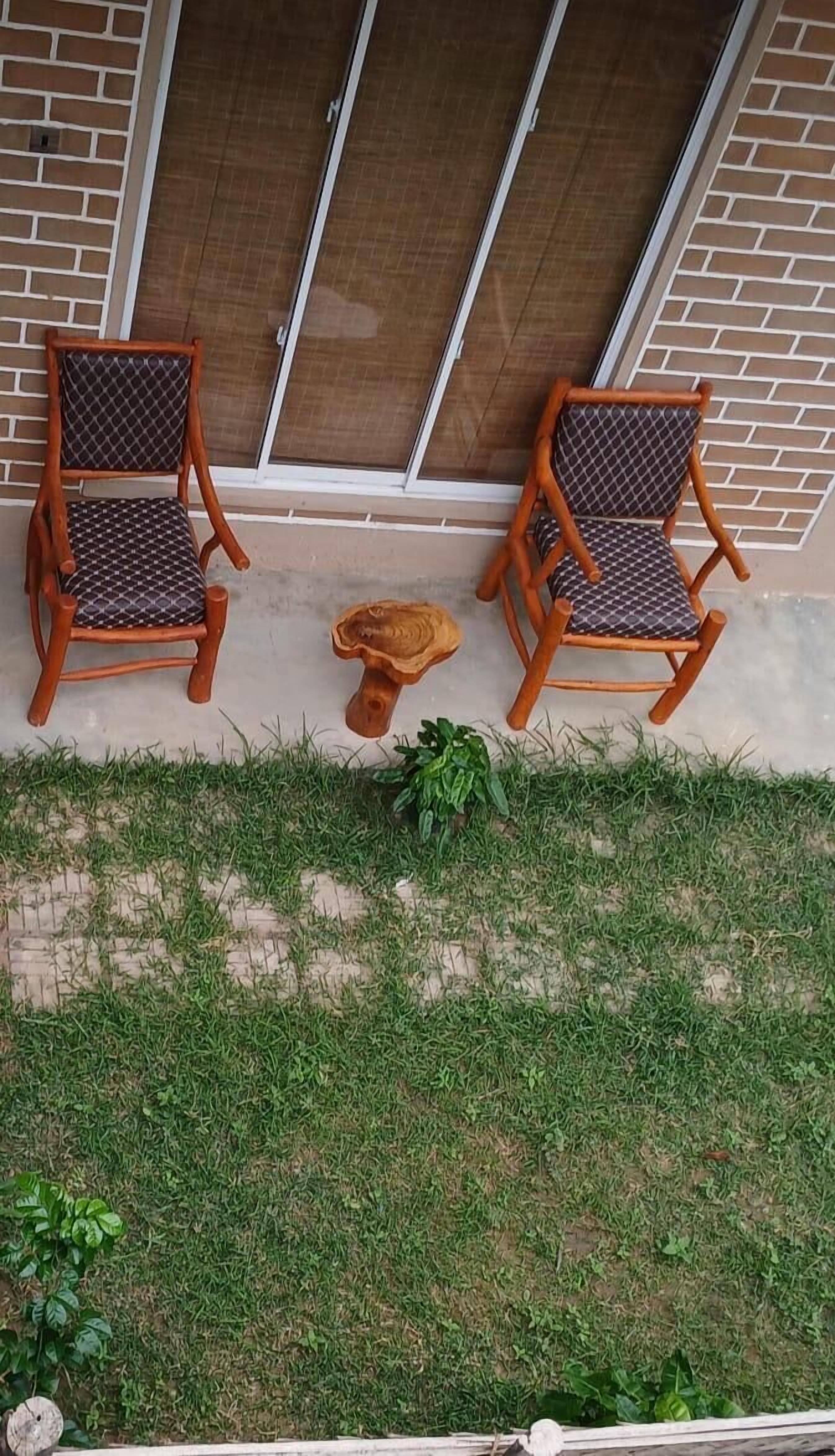 Two wooden chairs with patterned cushions placed on a concrete ledge outside a building with a brick wall and a glass door.