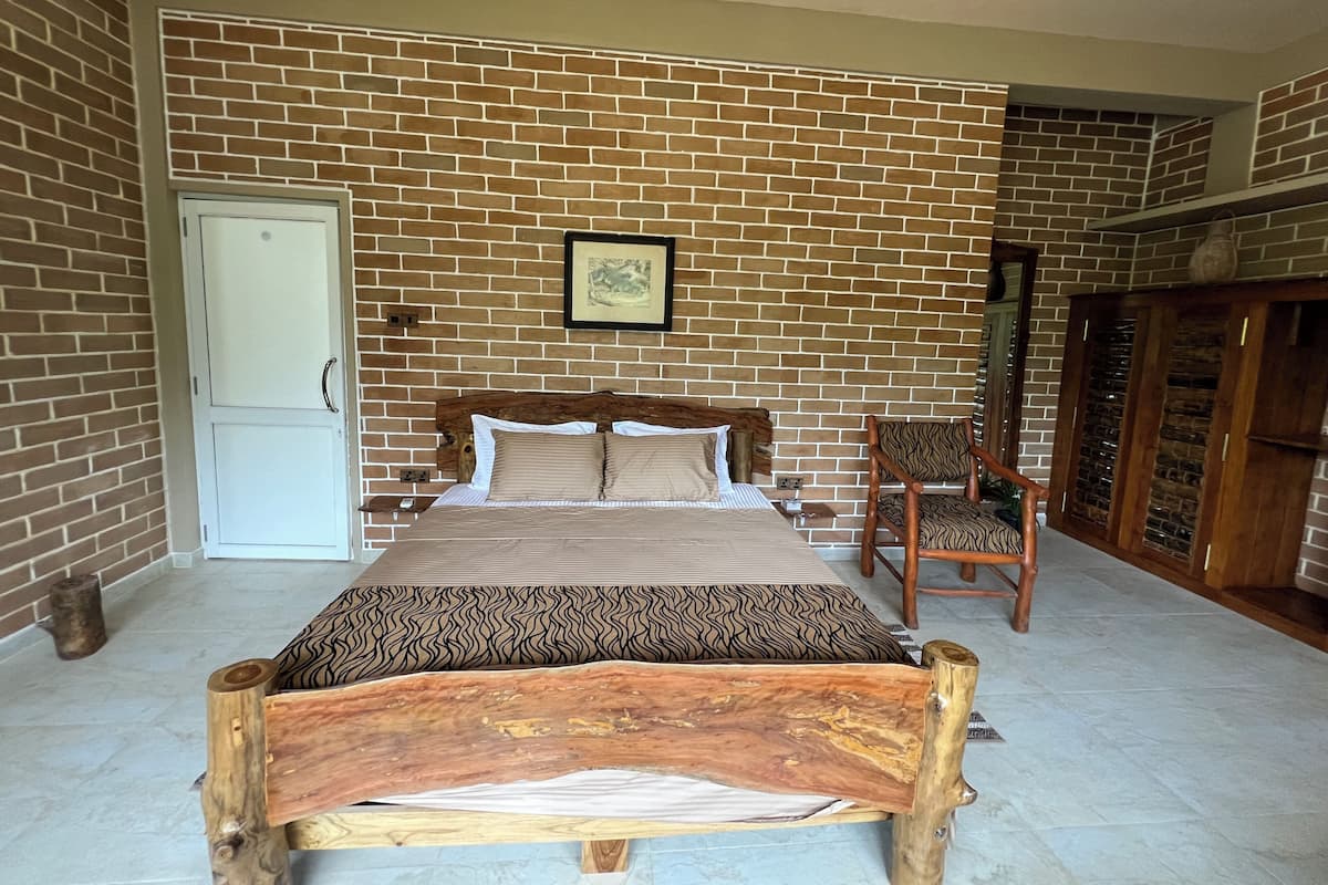 Un dormitorio con pared de ladrillo, estructura de cama de madera, una silla y un armario.