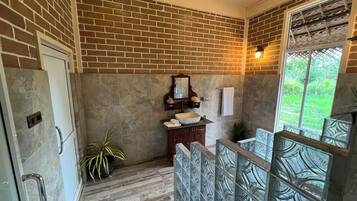Un baño con pared de ladrillo, tocador de madera, un espejo grande y una ventana con vistas a la vegetación.