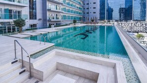 A modern hotel with a large indoor swimming pool, a well-maintained garden area, and a view of the city skyline. - GLOBALSTAY. DAMAC Majestine Apartments (Dubai)