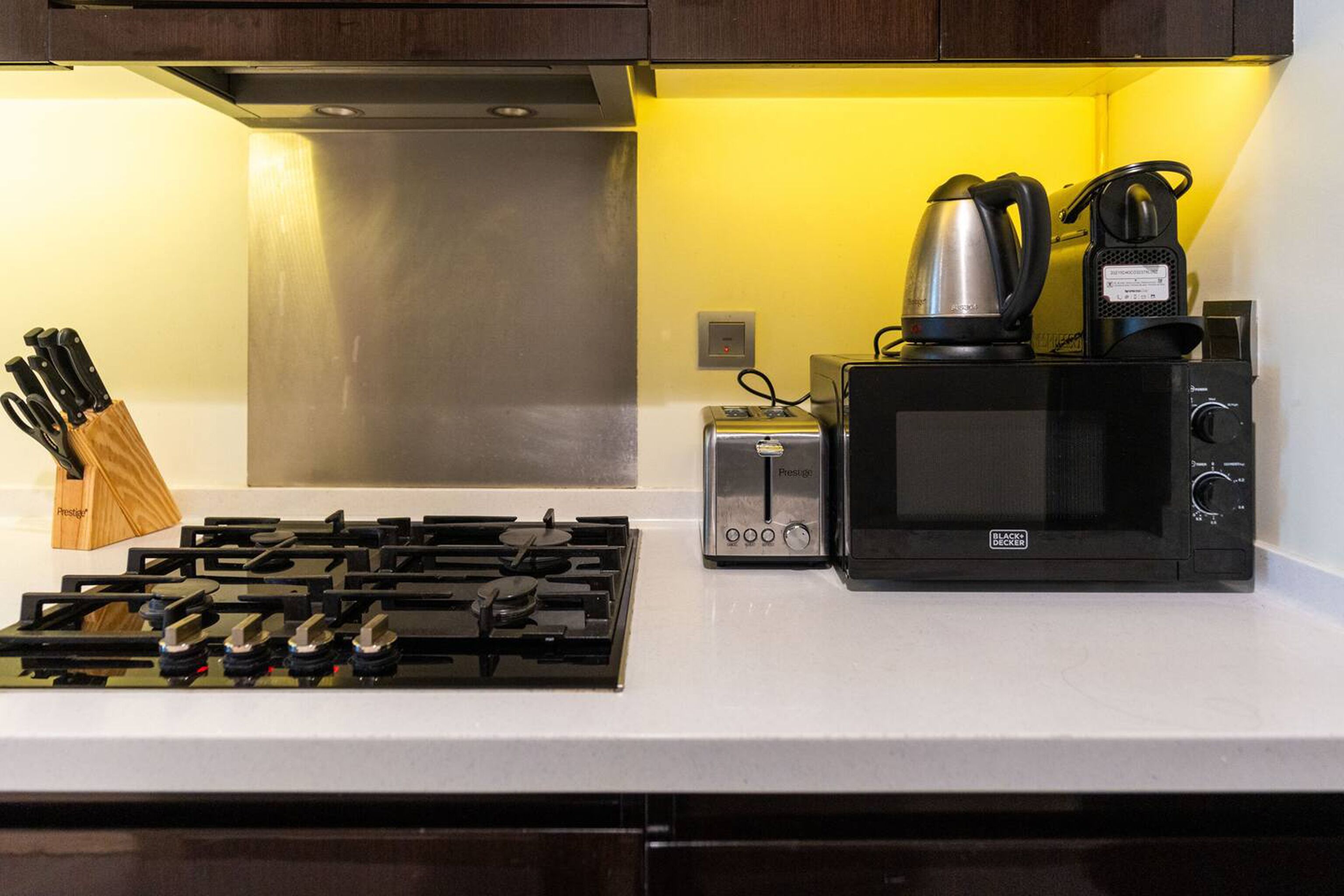 A kitchen with a gas stove, a toaster, a kettle, and a microwave.
