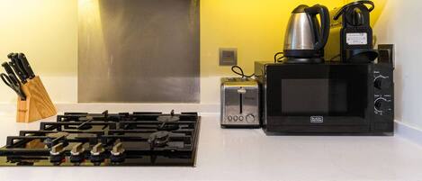 A kitchen with a gas stove, a toaster, a kettle, and a microwave.