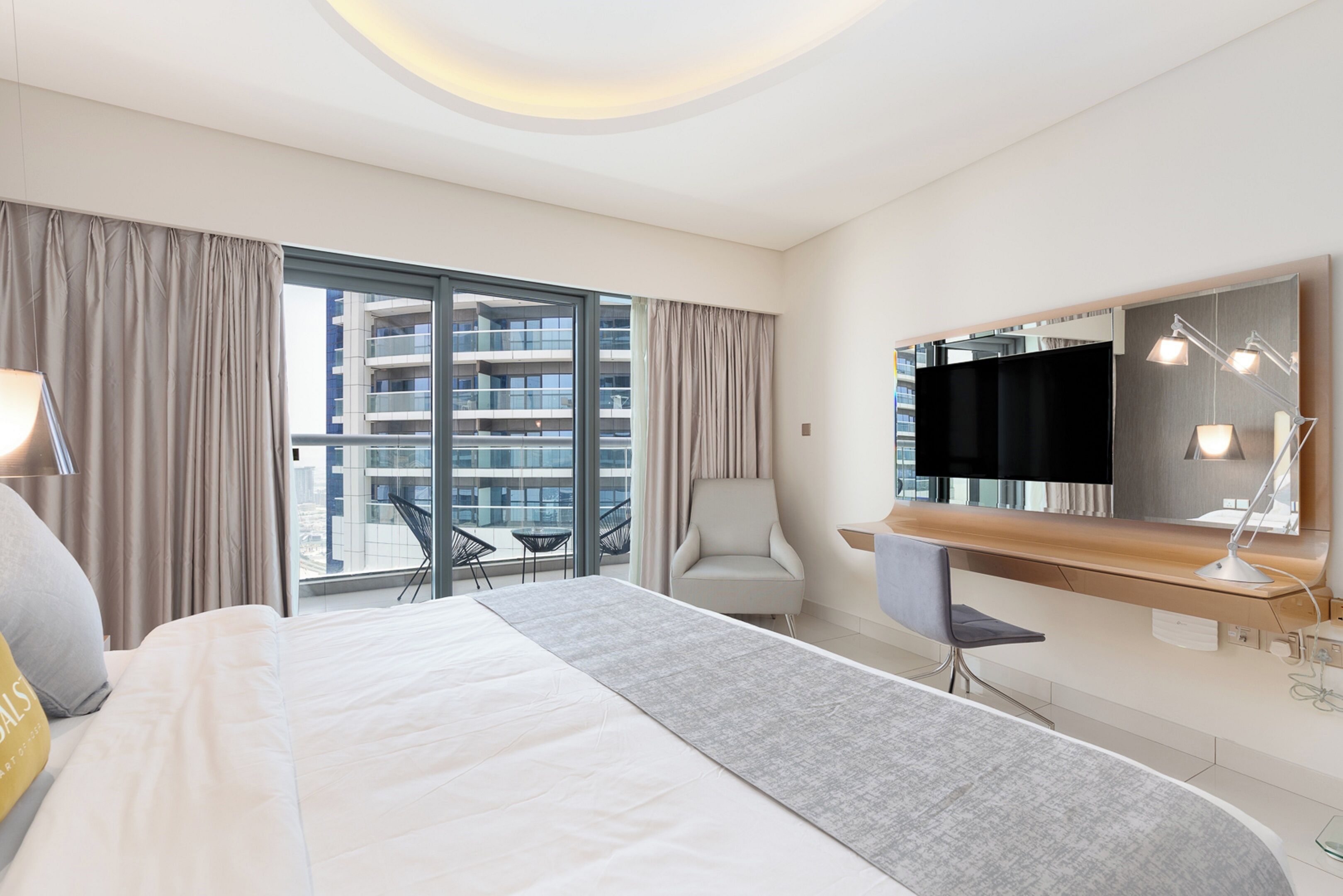 Una camera d'albergo moderna con un letto grande, una scrivania, una sedia, una TV e un balcone con vista sulla città.