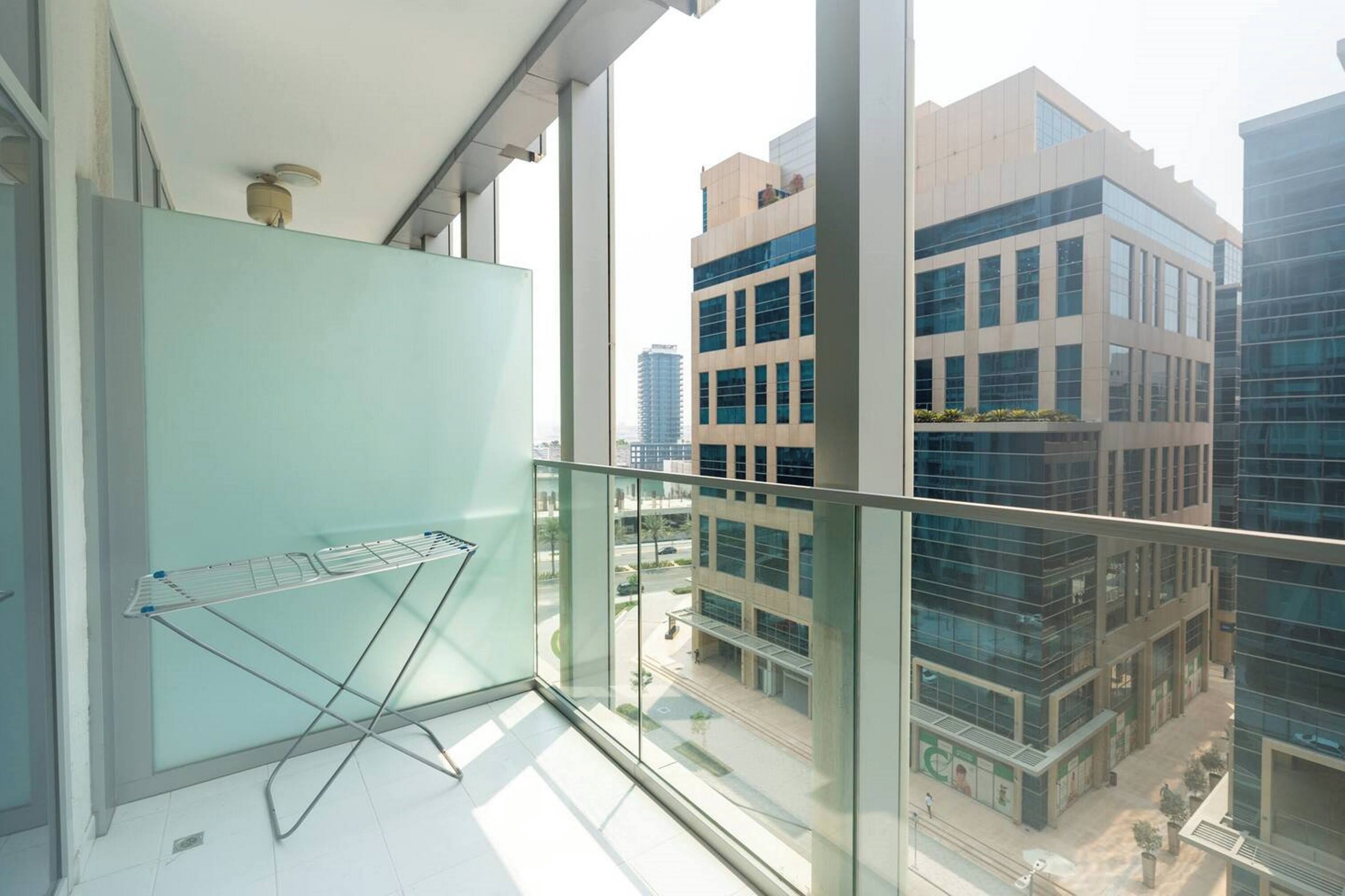 A balcony with a metal drying rack, large windows, and a view of modern buildings.