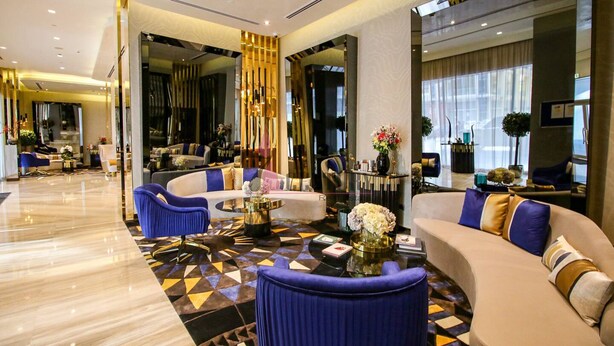 A modern hotel lobby with a marble floor, a curved sofa, and a seating area with blue chairs. - GLOBALSTAY. DAMAC Majestine Apartments (Dubai)