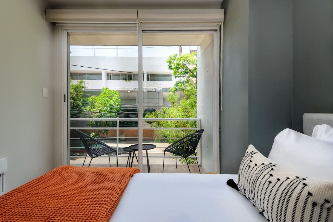 Een hotelkamer met een bed, een groot raam en een balkon met stoelen en een tafel.