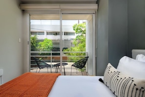 Habitación de hotel con una cama, un ventanal grande y un balcón con sillas y una mesa.