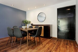 Ein Essbereich mit Holztisch, vier Stühlen, einer Topfpflanze und einem runden Spiegel an der Wand.