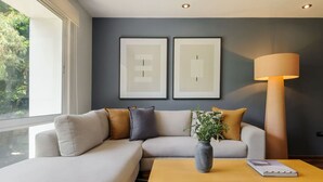 Ein modernes Wohnzimmer mit einer Couch, einem Couchtisch und einer Lampe. Zwei gerahmte Kunstwerke hängen an der Wand.