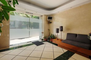 Ein Empfangsbereich mit einer Couch, einem an der Wand befestigten Fernseher und einem gefliesten Boden.