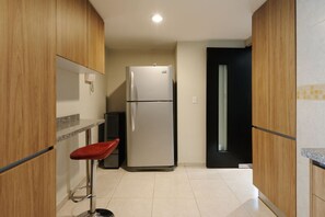 Eine kleine Küche mit Holzausbau, einem Edelstahlkühlschrank, einem roten Barhocker und einer schwarzen Tür.