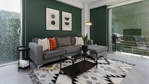 A modern living room with a grey sofa, black coffee table, and a patterned rug. There are two framed artworks on the wall, a floor lamp, and a view of greenery outside. - Stylish 2-Bdr Haven with Relaxing Balcony (Ciudad de México)