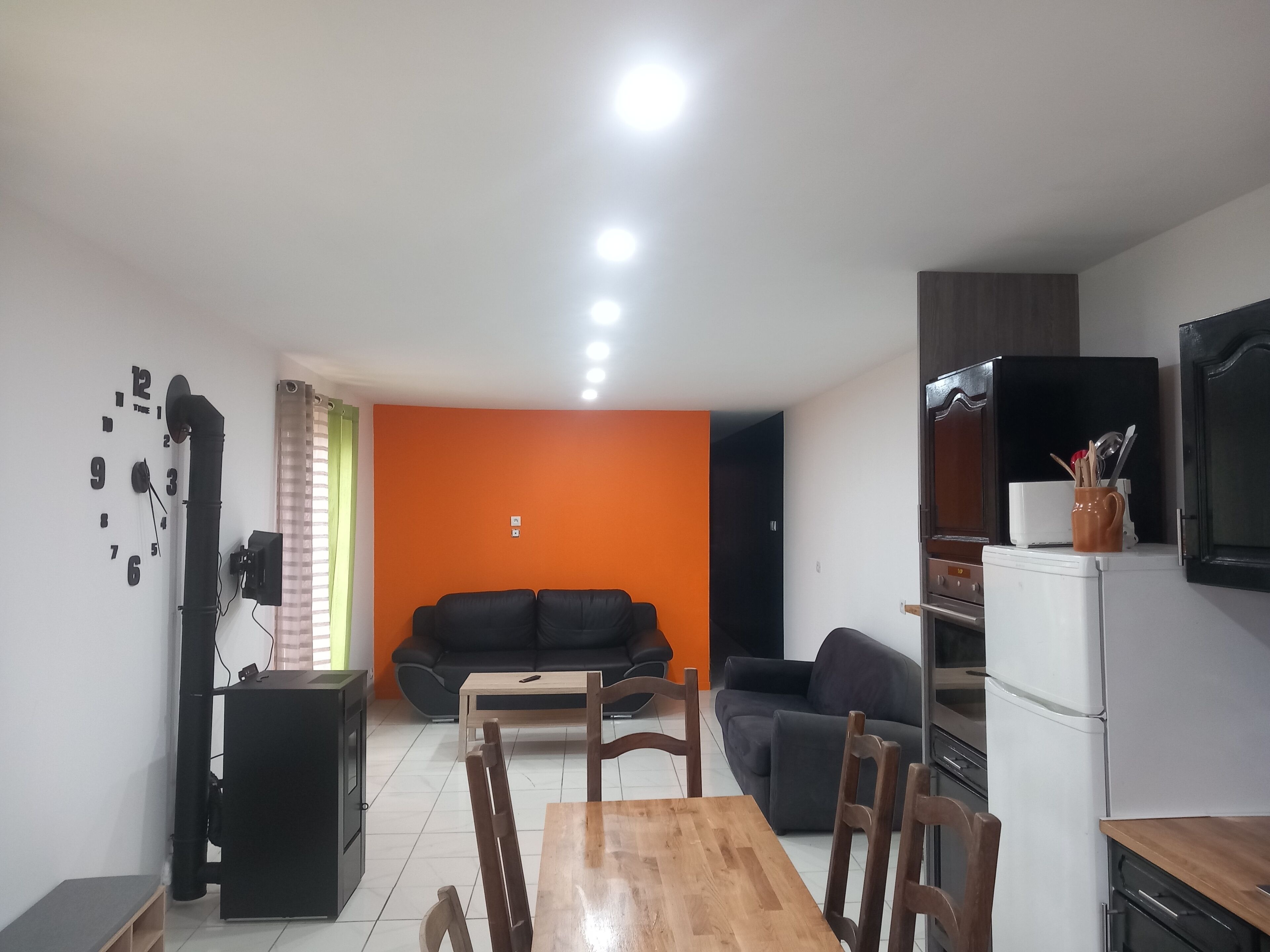 Ein gemütlicher Wohnbereich mit Essplatz, zwei Sofas, einer Küche inklusive Kühlschrank und einem an der Wand montierten Fernseher.