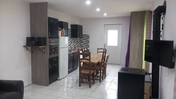 A modern kitchen with dark cabinets, a white refrigerator, and a dining area with wooden chairs and a table.