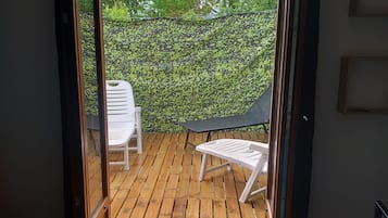 A room with a bed, a wooden deck, a white chair, and a black lounge chair.