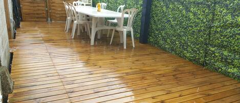 Una terraza de madera con una mesa y sillas, rodeada por una valla de madera y un muro de follaje verde.