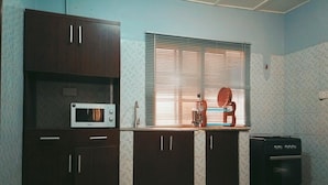 A kitchen with dark wooden cabinets, a microwave, a stove, and a window with blinds. - Vintage Classic Suites (Lekki)