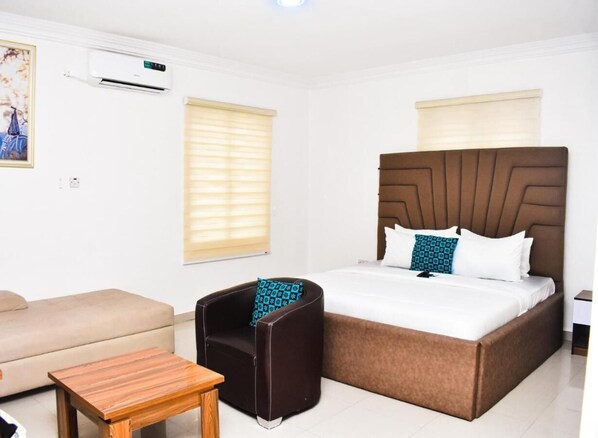A hotel room with a bed, a sofa, a small table, and a chair. - Vintage Classic Suites (Lekki)