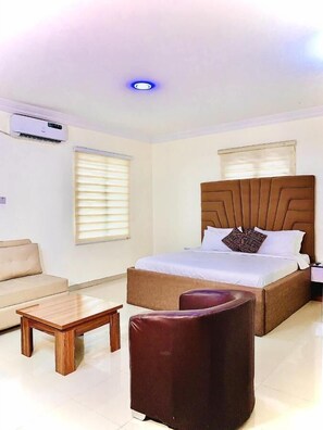 A hotel room with a bed, a sofa, a small table, and a chair. - Vintage Classic Suites (Lekki)