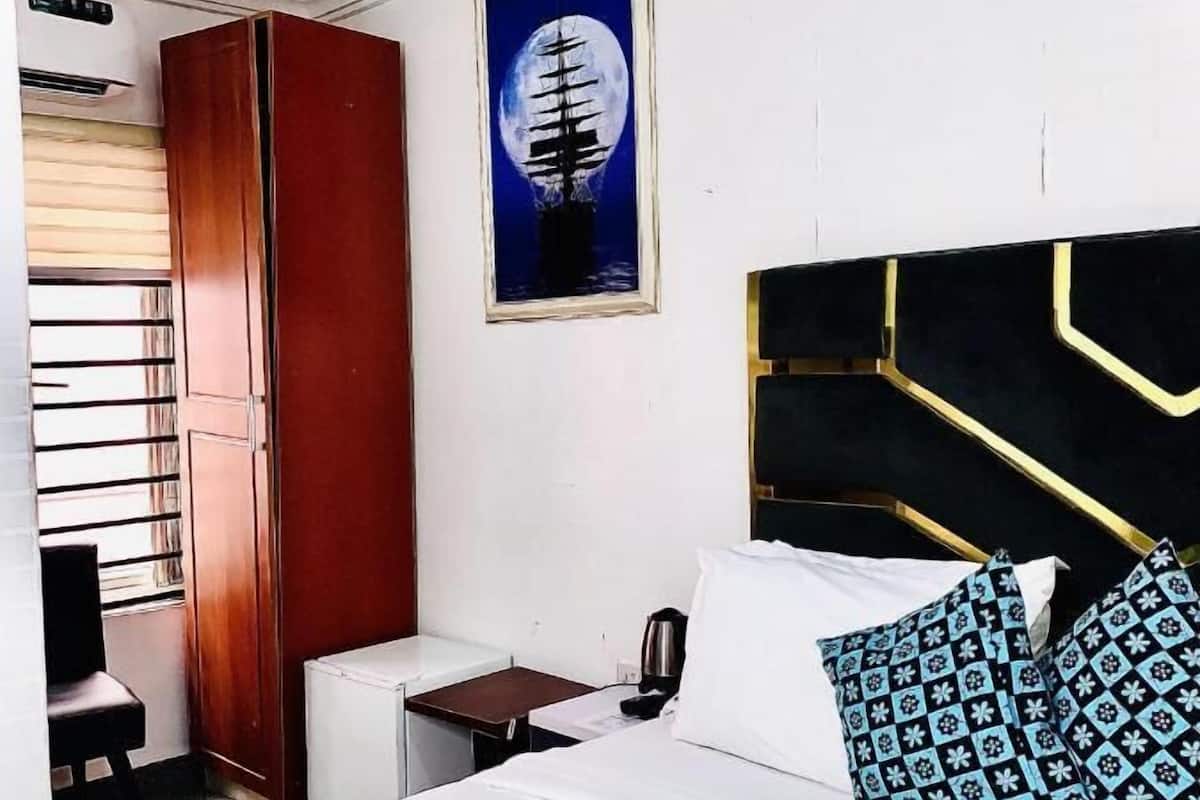 A hotel room with a bed, a desk, a wardrobe, and a painting of a ship on a moonlit sea.
