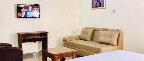 A hotel room with a bed, a sofa, a small table, a TV, and an air conditioning unit.
