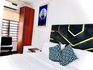 A hotel room with a bed, a desk, a chair, a wardrobe, and a framed picture on the wall. - Vintage Classic Suites (Lekki)