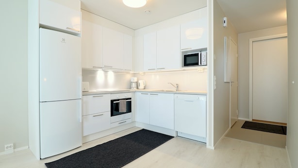 Eine moderne Küche mit weißen Schränken, einem Backofen, einer Mikrowelle und einer Kaffeemaschine.