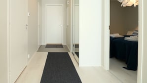 Ein Korridor mit dunklem Teppichboden, der zu einem Zimmer mit einem Bett und einem Nachttisch führt.
