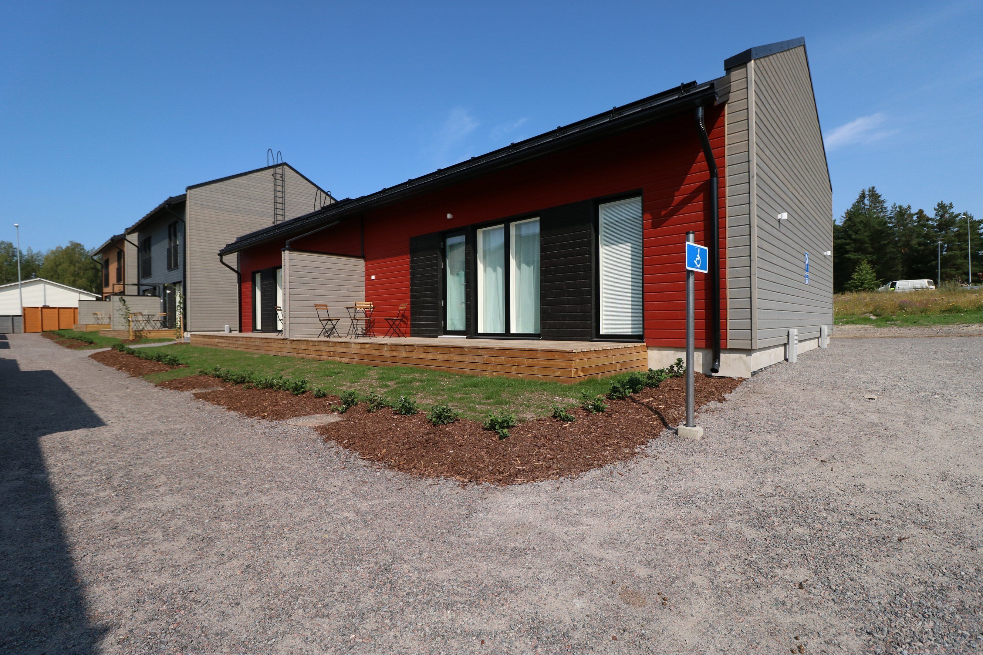 A modern two-story building with a red facade, large windows, and a covered porch.