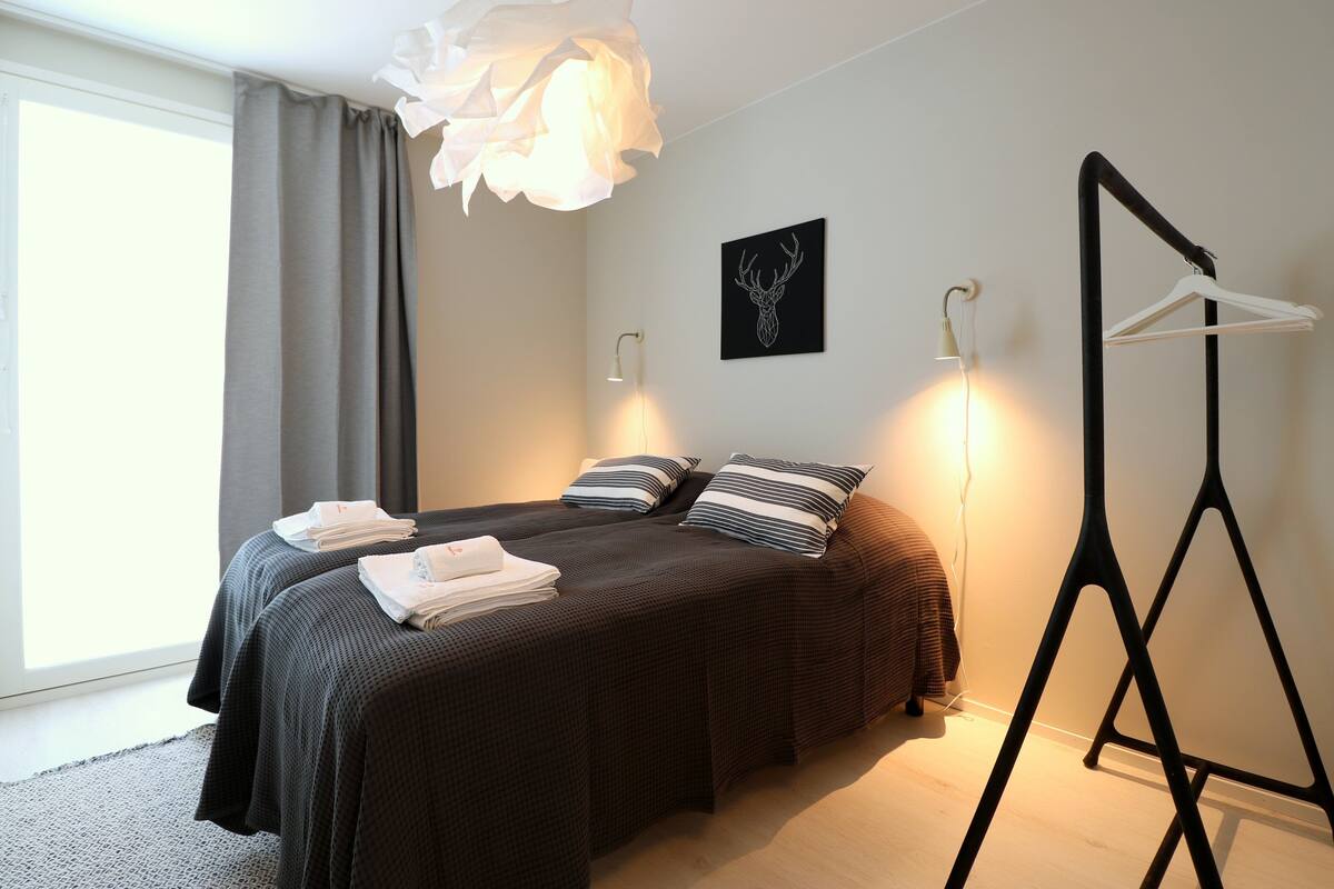 Una moderna camera d'albergo con un letto grande, due abat-jour, un'opera d'arte in bianco e nero sulla parete e un appendiabiti.