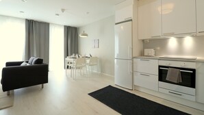 Eine moderne Küche mit weißen Schränken, einem eingebauten Ofen und einer Mikrowelle. Im Wohnbereich befindet sich ein Esstisch mit Stühlen und eine schwarze Couch.
