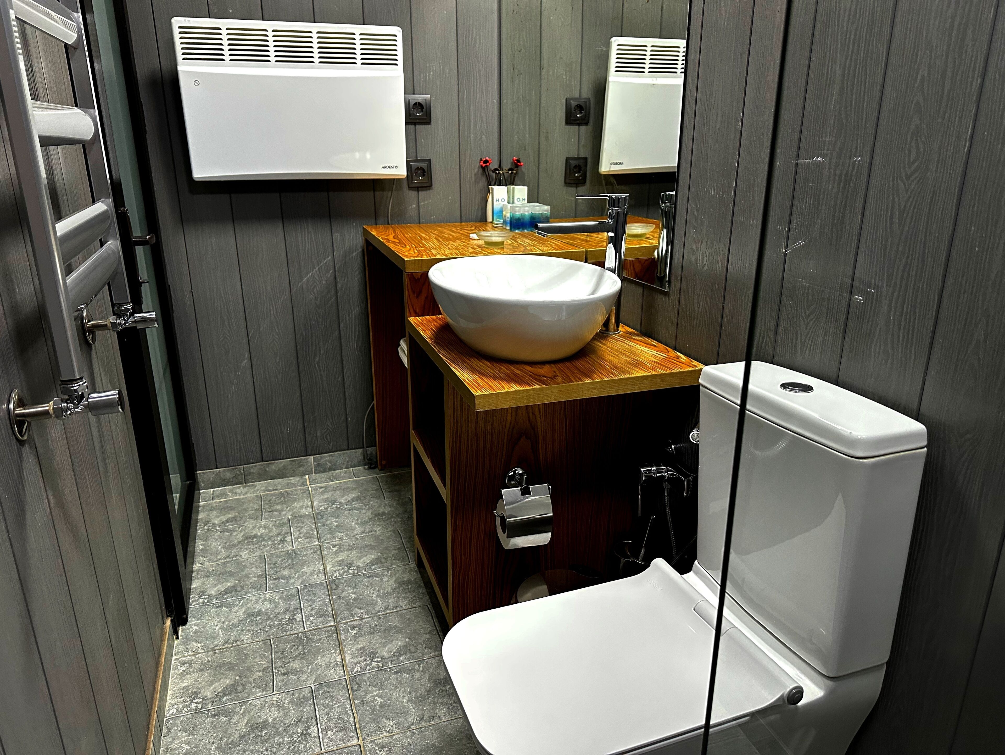 A compact bathroom with a white toilet, a wooden vanity with a large sink, and two wall-mounted air conditioners.
