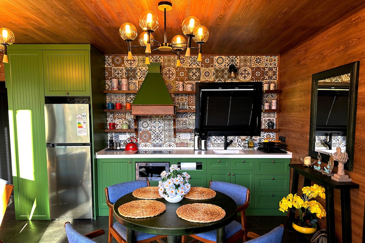 Een keuken met groene kastjes, een zwart aanrecht en een ronde tafel met blauwe stoelen.