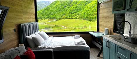 Un dormitorio con un ventanal grande, una cama, un sofá y una mesita con un hervidor.