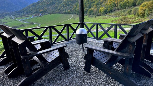 En træterrasse med Adirondack-stole med udsigt over en naturskøn dal med en flod og bjerge.