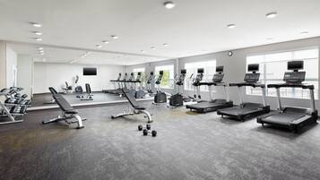 A modern gym with various exercise equipment, large windows, and a clean, spacious layout.