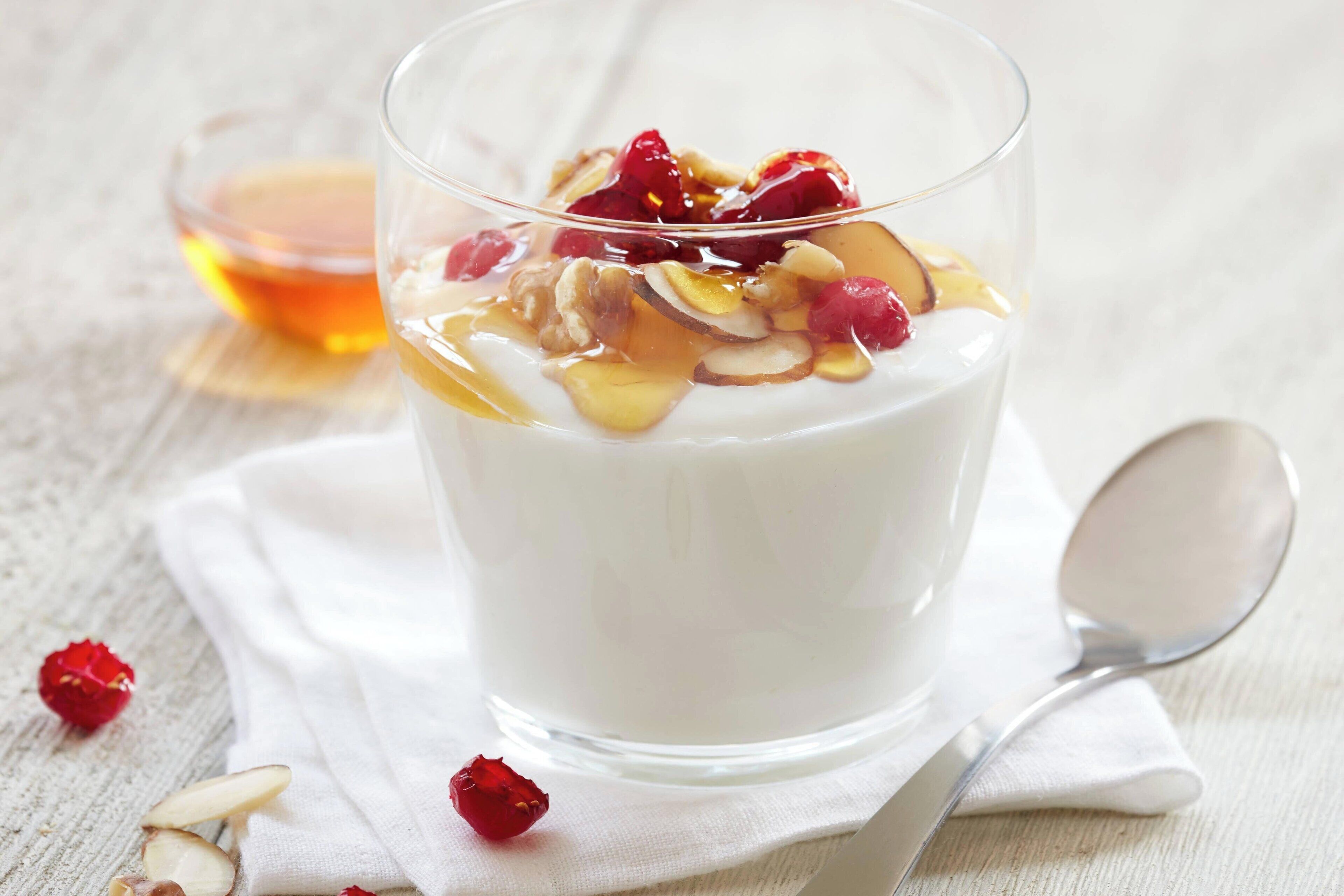 Un vaso de yogur cubierto de frutas y nueces, una cuchara y un tazón pequeño de miel.