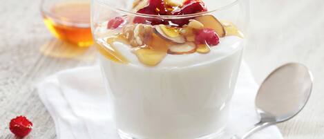Un vaso de yogur cubierto de frutas y nueces, una cuchara y un tazón pequeño de miel.