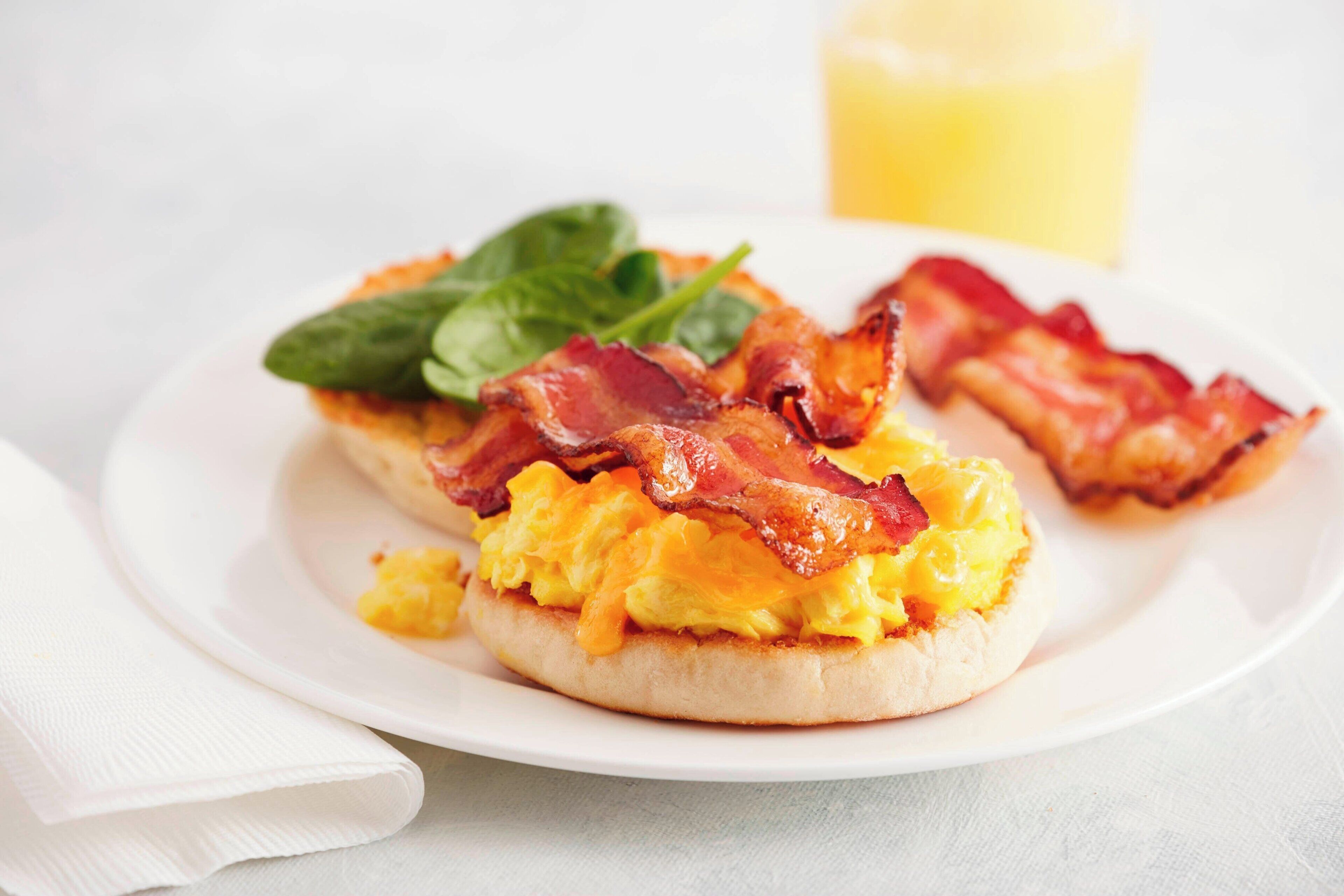Un plato de desayuno con huevos revueltos, tocino y espinacas sobre un plato blanco.