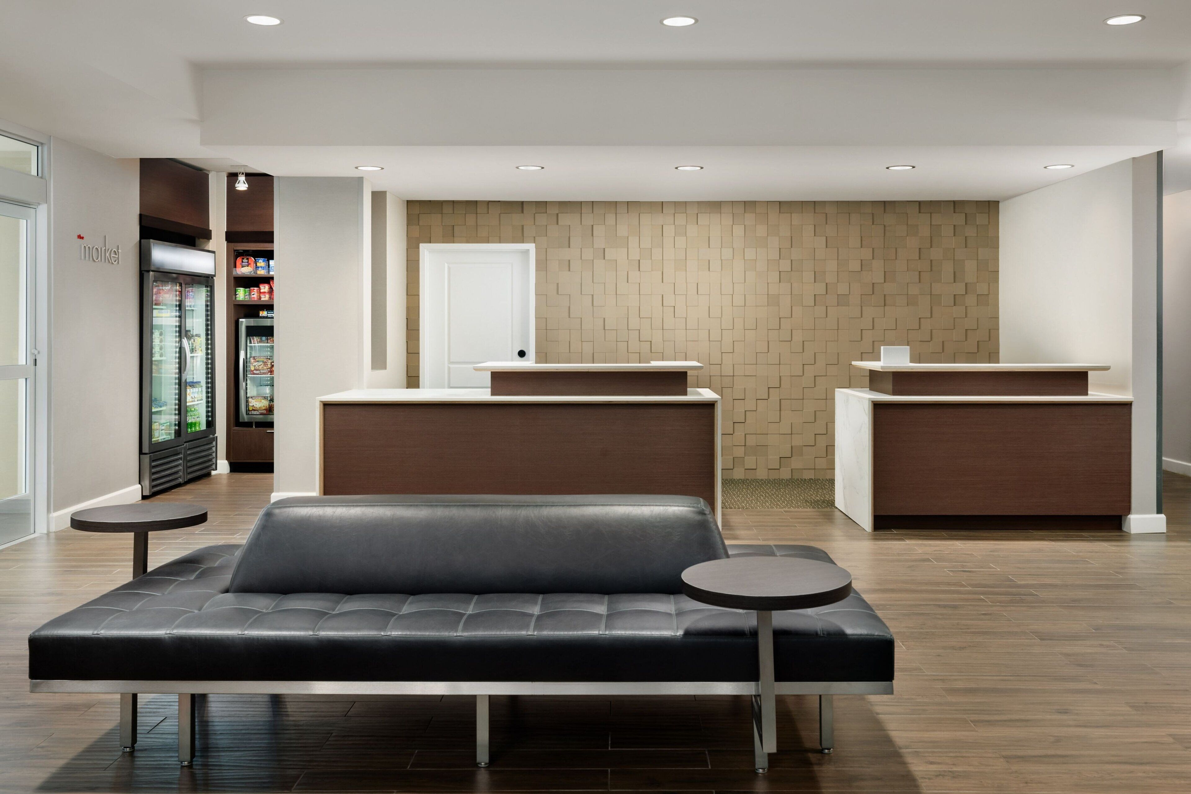 Um hall de hotel moderno com balcão de recepção, área de espera com sofá e refrigerador cheio de bebidas.