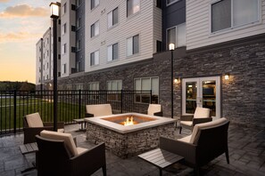 A patio with a stone fire pit, wicker furniture, and a view of a multi-story building with windows and outdoor lighting. - Residence Inn King of Prussia (King of Prussia)